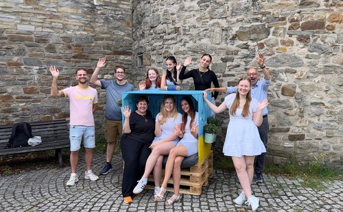 Strandkorb mit drei sitzenden Menschen und  Gruppe junger Menschen dahinter