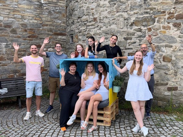 Strandkorb mit drei sitzenden Menschen und  Gruppe junger Menschen dahinter