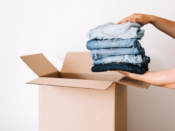 Zwei Hände legen einen Stapel Hosen in einen Papp-Karton