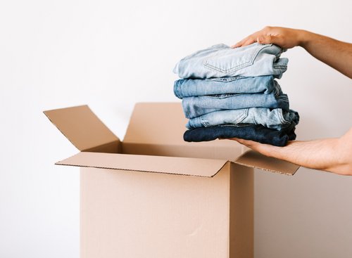 Zwei Hände legen einen Stapel Hosen in einen Papp-Karton