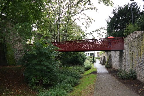 Rote Stahlbrücke mit durchlöcherter Brüstung über dem Stadtgraben