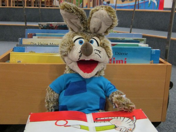 Eine Stoffpuppe mit Hasenohren sitzt vor einem offenen Buch