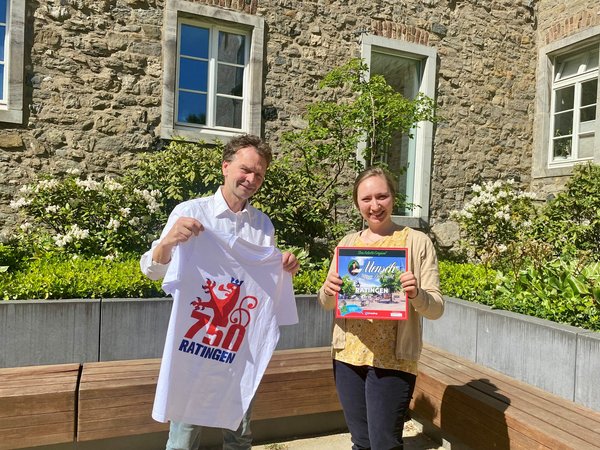 Mann hält ein T-Shirt in den Händen, daneben steht eine Frau mit einem Spiel