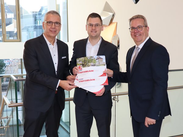 Drei Männer in schwarzen Anzügen mit einer Broschüre in der Hand