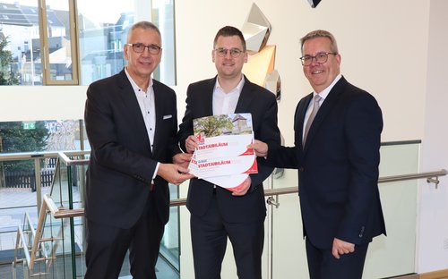 Drei Männer in schwarzen Anzügen mit einer Broschüre in der Hand