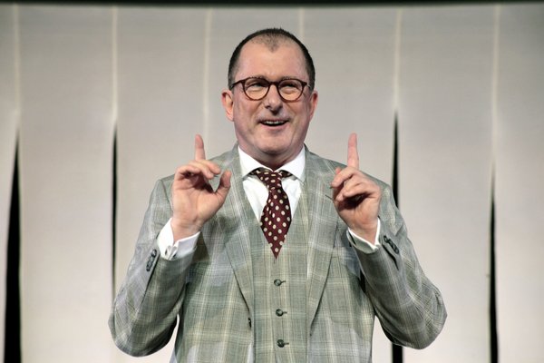 Schauspieler im Jackett und zwei gehobenen Zeigefingern