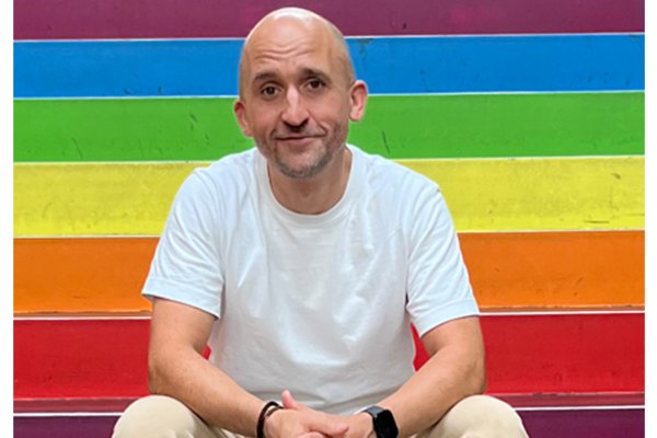 Markus Barth, sitzend vor einer Regenbogenfahne