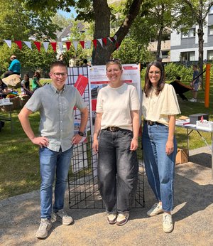 Das Foto zeigt zwei Frauen und einen Mann, die vor einem Informationsstand stehen. 