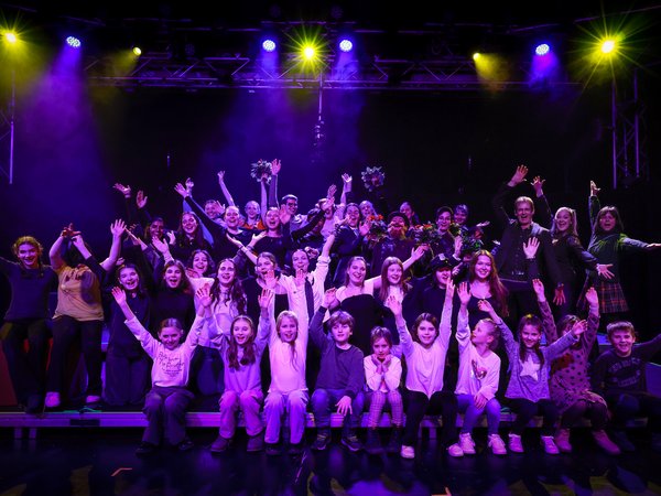 Personengruppe auf einer Bühne reißt die Arme in die Höhe