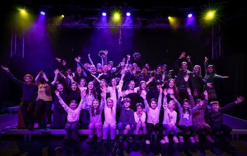 Personengruppe auf einer Bühne reißt die Arme in die Höhe