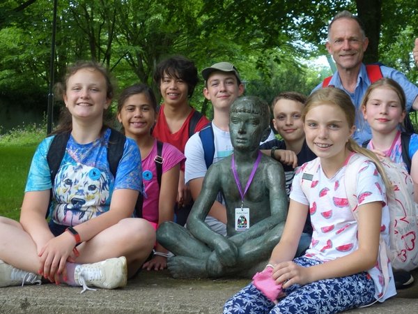 Mehrere Kinder und ein Mann hocken neben einer Bronzefigur