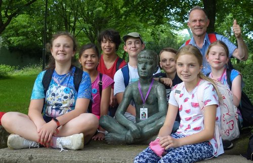 Mehrere Kinder und ein Mann hocken neben einer Bronzefigur