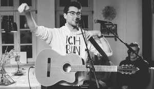 Junger Sänger mit einer Gitarre und weißem Pullover (schwarz-weiß Foto)