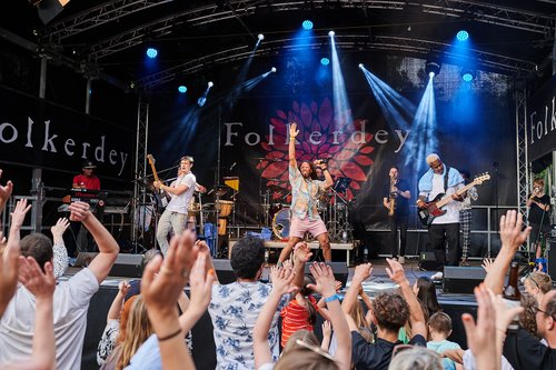 Band auf einer Bühne, davor reißen Menschen die Hände in die Höhe