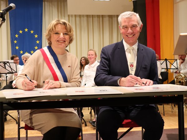 Mann und Frau sitzen an einem Tisch mit Füller in der Hand, vor ihnen liegen Dokumente