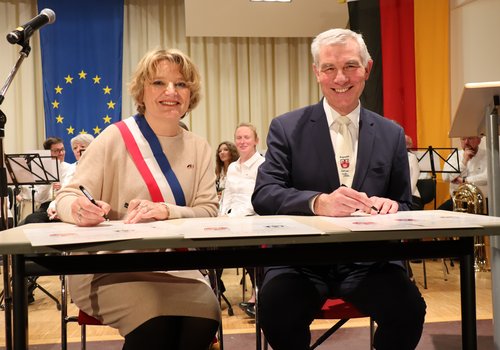 Mann und Frau sitzen an einem Tisch mit Füller in der Hand, vor ihnen liegen Dokumente