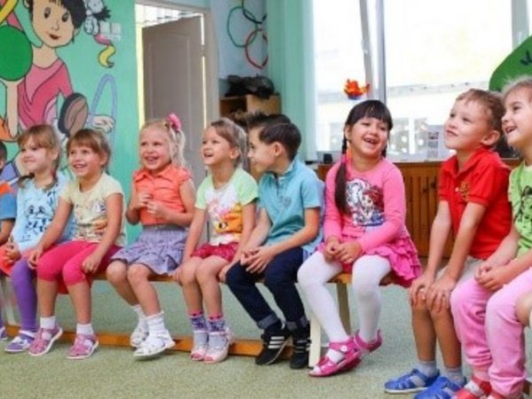 Kinder sitzen in einer Kita nebeneinander auf Stühlen