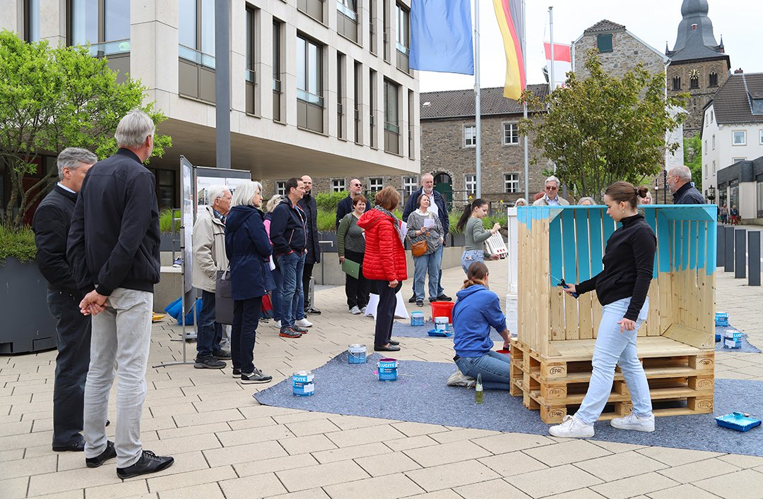 Gruppe von Menschen auf dem Rathausplatz und Jugendliche die zwei Strandkörbe gestalten.