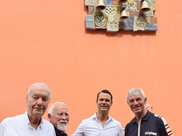 Mehrere Personen vor einem Glockenspiel an einer Hauswand.