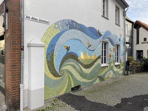 Das Foto zeigt ein buntes Wandmosaik an einer Hausfassade in der "Am alten Steinhaus" Straße.