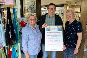 Kunstrally in Ratingen - Drei Personen halten ein Schild mit einer Ankündigung für die Kunstrally Ratingen im Jahr 2022 in die Kamera.