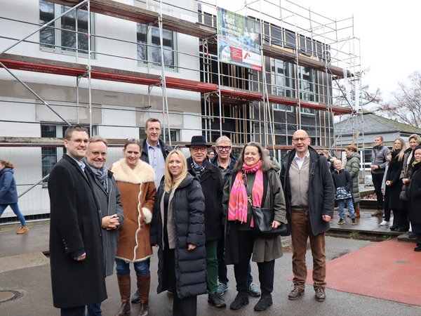 Gruppe von Menschen vor einem eingerüsteten Gebäude im Rohbau