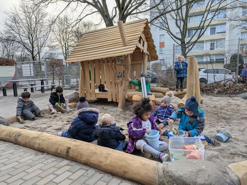 Kinder spielen im Sand, dahinter ein Spielhaus aus Holz
