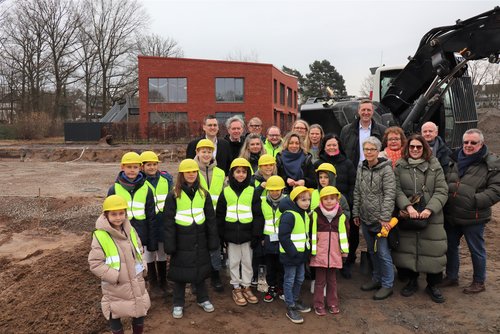 Kinder mit Bauhelmen sowie mehrere Personen auf einem Baufeld  