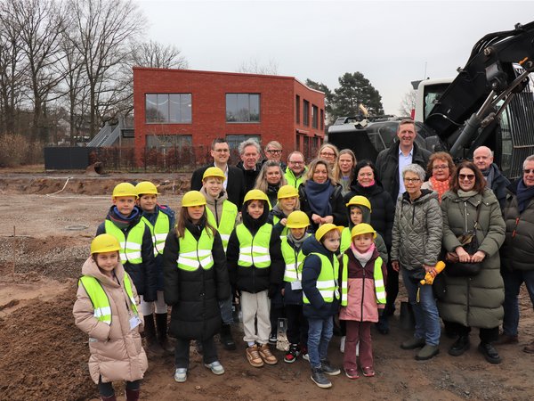 Kinder mit Bauhelmen sowie mehrere Personen auf einem Baufeld  