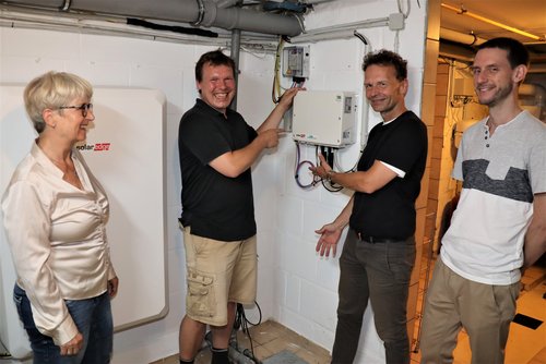 Drei Männer und eine Frau vor Solartechnikgeräten im Keller