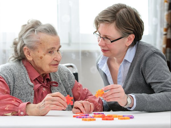 Eine alte und eine jüngere Frau sitzen an einem Tisch und halten Puzzlezeile in den Händen