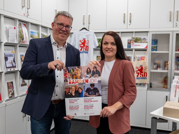 Mann und Frau halten ein Veranstaltungsplakat in den Händen