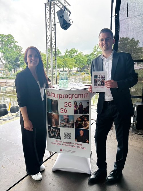 Ein Mann und eine Frau stehen mit Poster auf einer Bühne