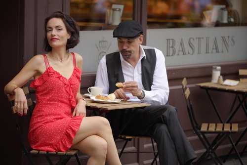 Frau in rotem Kleid und Mann mit Baskenmütze sitzen an einem kleinen Tisch