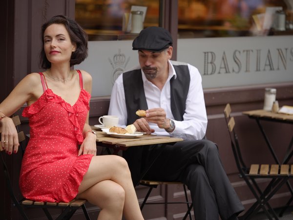 Frau in rotem Kleid und Mann mit Baskenmütze sitzen an einem kleinen Tisch