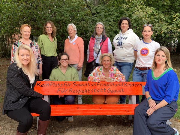 Zehn Frauen an einer orangefarbenen Sitzbank