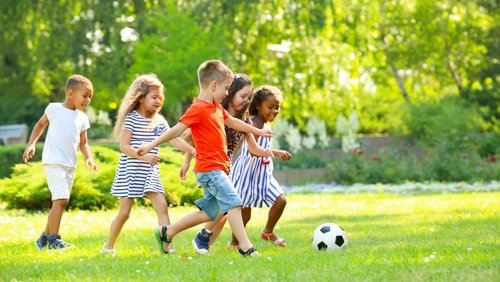 Kinder laufen auf einer Wiese einem Fußball hinterher