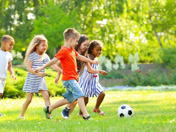 Kinder laufen auf einer Wiese einem Fußball hinterher