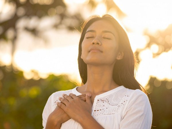 Frau mit geschlossenen Augen hält sich Hände gekreuzt vor der Brust  