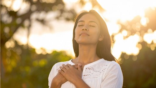 Frau mit geschlossenen Augen hält sich Hände gekreuzt vor der Brust  