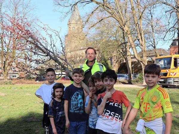 Mehrere Kinder und ein Mann halten einen jungen Baum