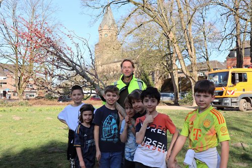 Mehrere Kinder und ein Mann halten einen jungen Baum