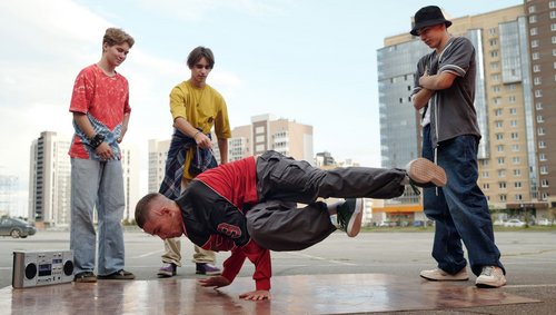 Vier Jugendliche, einer macht eine Breakedance-Figur auf dem Boden