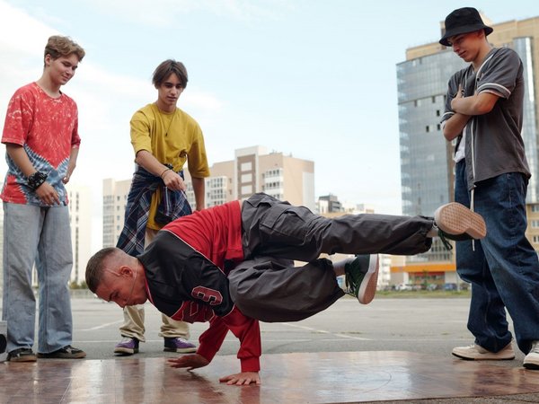 Vier Jugendliche, einer macht eine Breakedance-Figur auf dem Boden