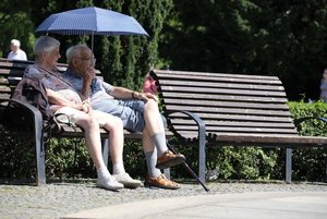 Ein älteres Paar auf einer Parkbank beschattet sich mit einem Regenschirm