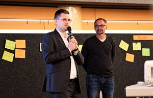 Mann mit Mikrofon, ein zweiter Mann steht daneben
