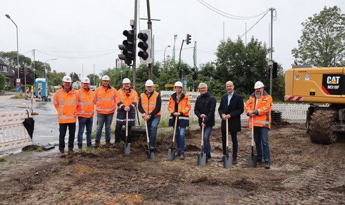 Mehrere Personen mit Helmen und Spaten auf einer Baustelle 
