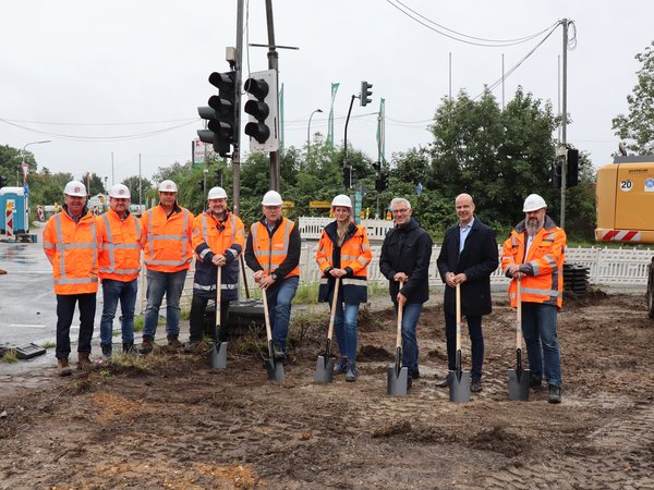 Mehrere Personen mit Helmen und Spaten auf einer Baustelle 