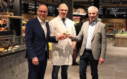 Drei Männer mit Sektgläsern in einem Lebensmittelladen