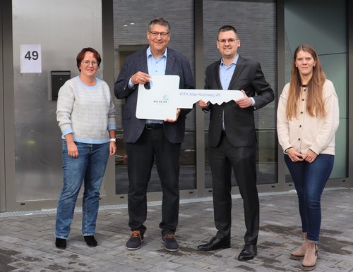 Vier Personen, zwei Männer halten einen überdimensionalen Schlüssel in den Händen